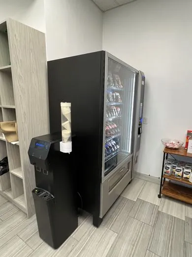 A snack and drink vending machine next to a water dispenser in a workplace kitchenette