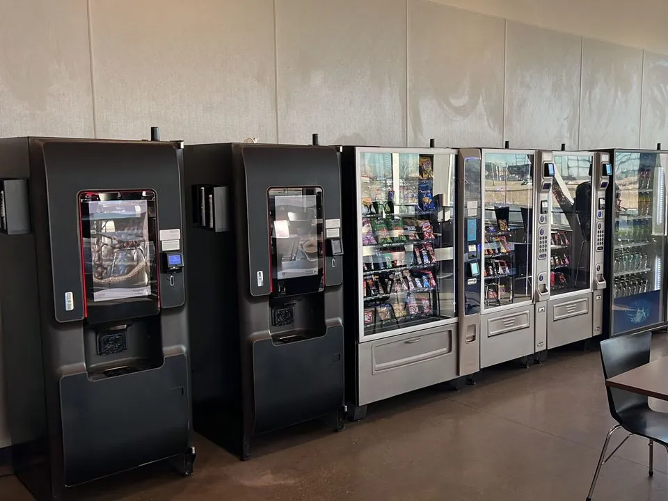 A row of hot beverage, snack and drink vending machines along the wall of a staff lunchroom