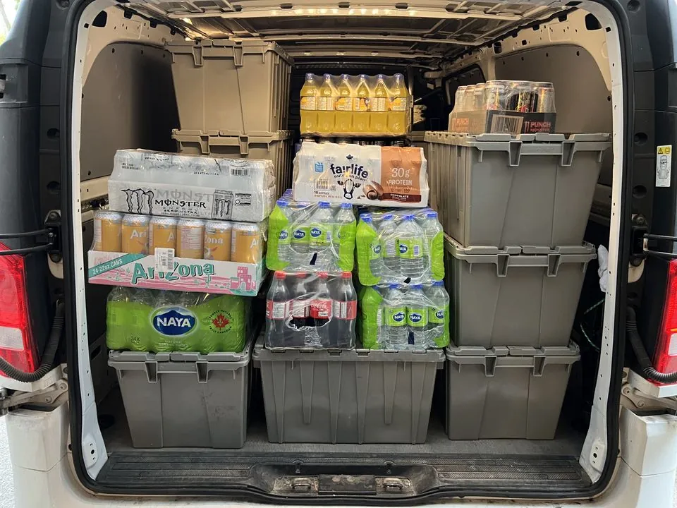 Cases of bottled drinks and grey restocking bins loaded in the back of a service van