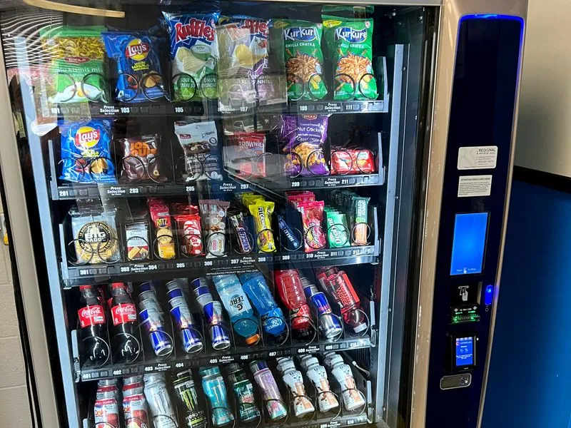 A stocked Regional Vending snack and drink machine with its service sticker and card payment reader